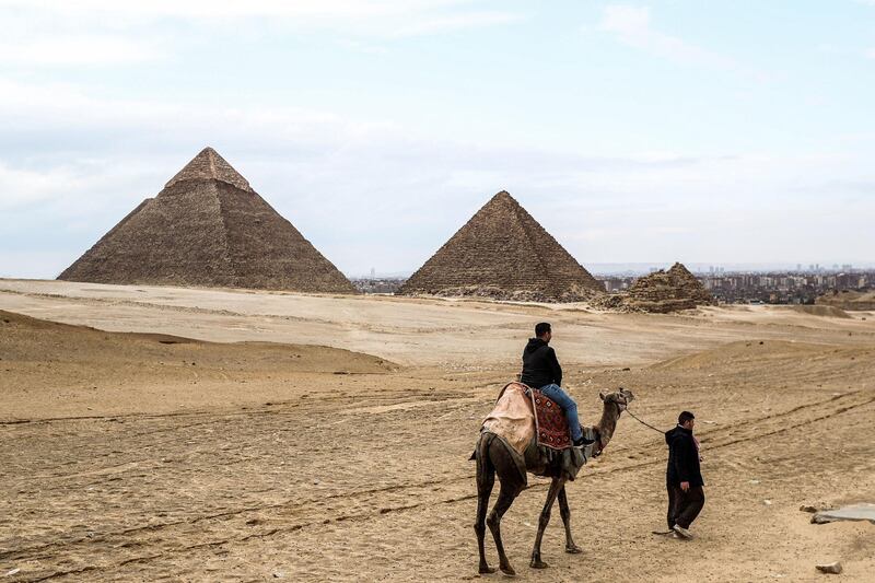 A camel guide leads a tourist on a camel at the Giza pyramids plateau overlooking the Giza necropolis on the southwestern outskirts of the Egyptian capital on March 13, 2020, as in the background are seen the Pyramid of Khafre (Chephren) and Menkaure (Menkheres). (Photo by Mohamed el-Shahed / AFP)