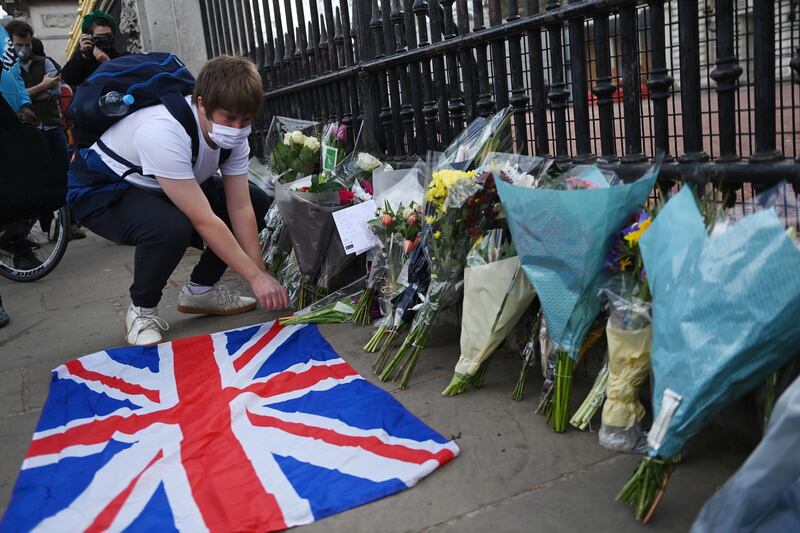 epa09124345 People place a Union Jack next to flowers outside Buckingham Palace. EPA