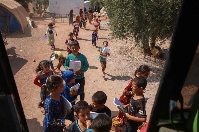 Displaced Syrian children queue for their turn outside a bus converted into a classroom.