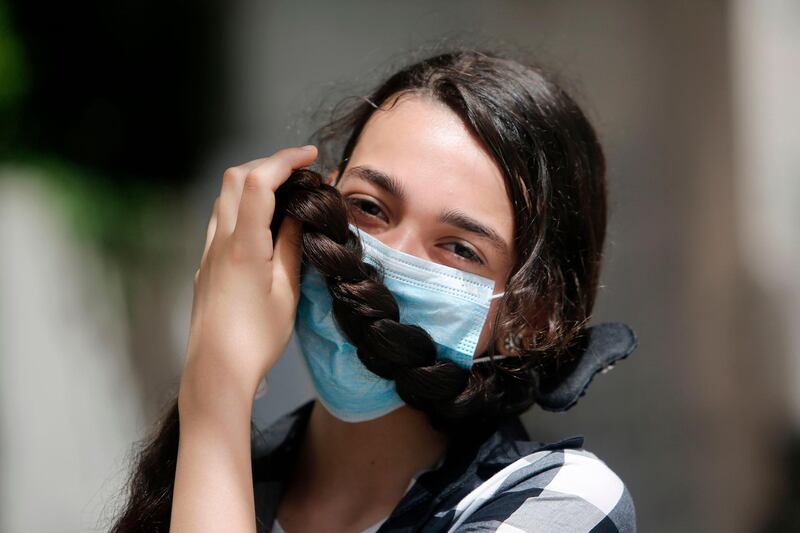 A Palestinian school girl holds up her braid before her mask as she stands inside a school in Gaza City.   AFP