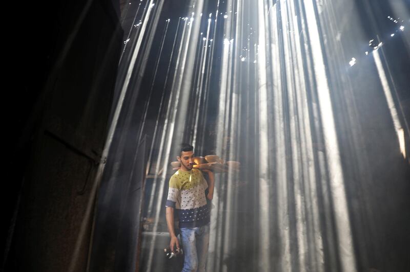 A Palestinian worker carries clay pots as the sun rays penetrate through the ceiling of a pottery workshop in Gaza City. Reuters