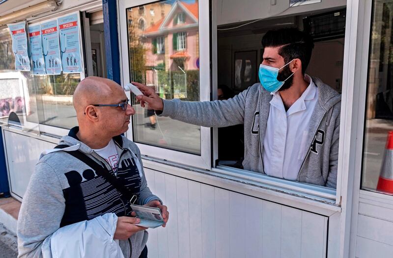 A Cypriot medic checks the temperature of a man crossing the Ledra Palace checkpoint in Nicosia on March 4, 2020, as the Greek Cypriot authorities started distributing pamphlets about the Covid-19 and checking people for the virus at checkpoints connecting the internationally-recognised Republic of Cyprus with the self-proclaimed Turkish Republic of North Cyprus, recognised only by Turkey, for the first time since the crossings opened in 2003. Cyprus announced the temporary closure of half of the crossing points across the divided island's ceasefire line last week in an effort to prevent a coronavirus outbreak.  / AFP / Iakovos Hatzistavrou
