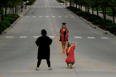 A woman wearing graduation attire is photographed in the middle of an empty street on the University of Kansas campus Sunday, April 26, 2020, in Lawrence, Kan. The campus has canceled in-person classes and is instead offering remote learning, as part of attempt to stem the spread of the new coronavirus. (AP Photo/Charlie Riedel)