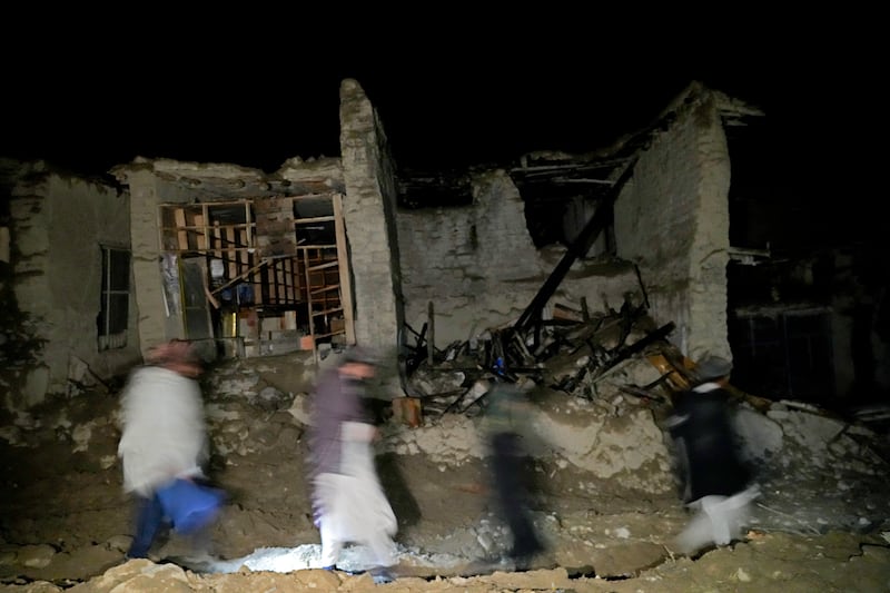 Afghans walk by a destroyed house in the village of Gyan. AP