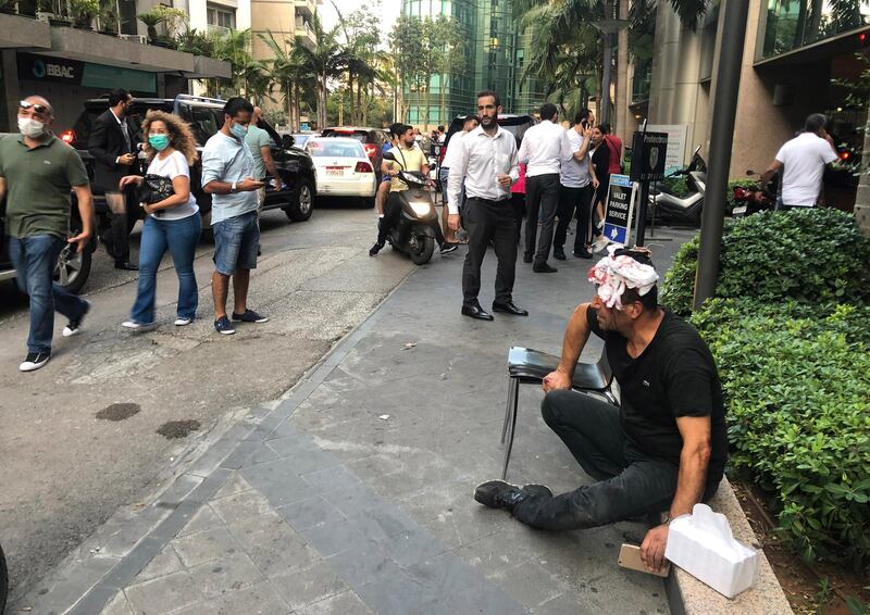 An injured man sits in shock on the pavement following an explosion at the Beirut port.  EPA