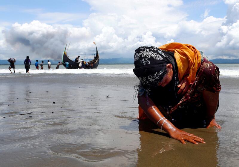 An exhausted Rohingya refugee woman touches the shore after crossing the Bangladesh-Myanmar border by boat through the Bay of Bengal, in Shah Porir Dwip, Bangladesh, 2017.