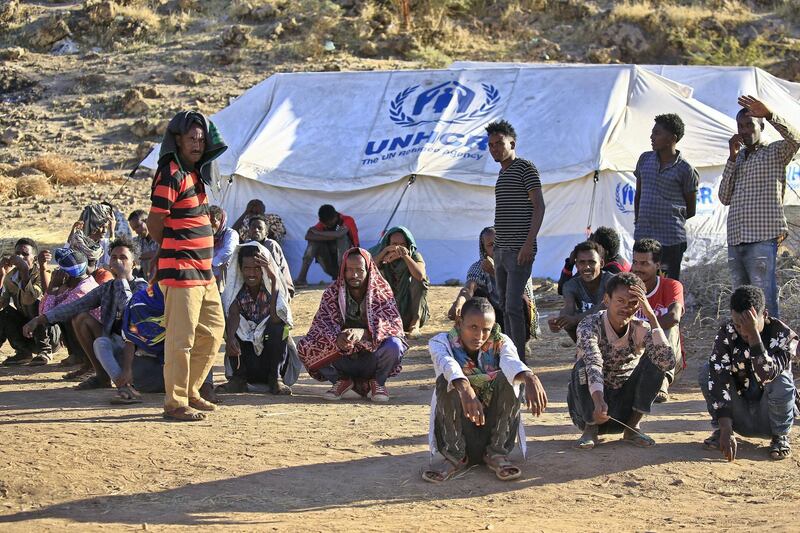 Ethiopian refugees wait outside a UNHCR tent for food prepared on Coptic Christmas day following the slaughtering of sheep for the occasion at Um Raquba refugee camp in Gedaref, eastern Sudan, on January 7, 2021. (Photo by ASHRAF SHAZLY / AFP)