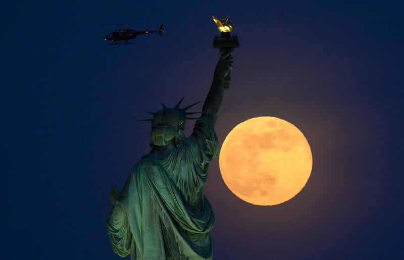 A helicopter flies past as the full moon rises behind the Statue of Liberty.  AFP