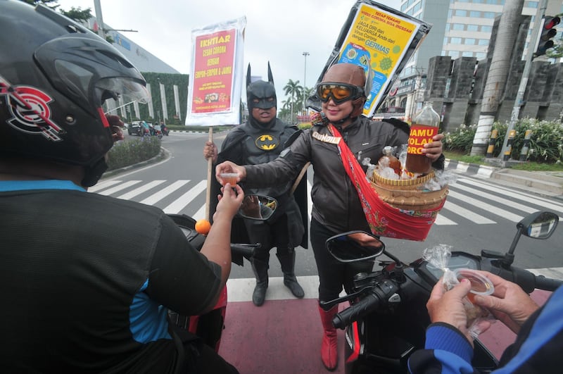 People wearing character clothes of local hero Gundala (right) and Batman (left) offer Indonesian traditional herbal drinks “Jamu” to motorists as they encourage them to stay healthy and fight COVID-19 in Solo, Indonesia. AFP