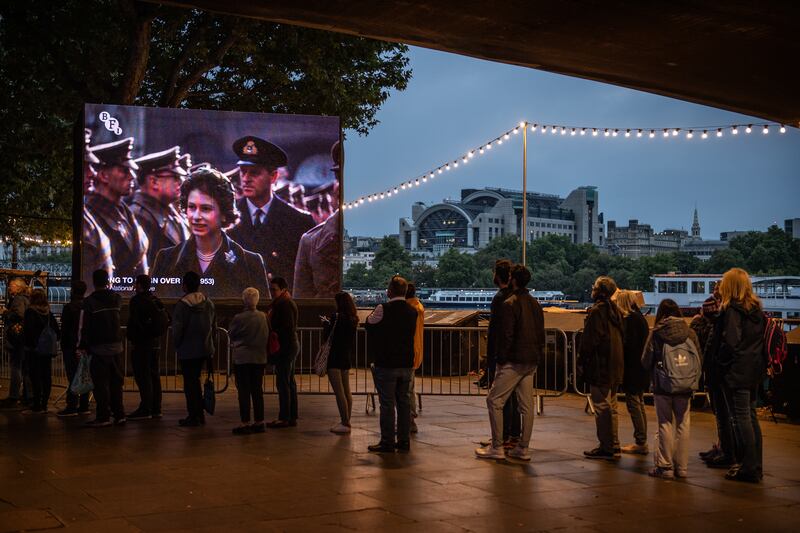 An outdoor screen on the South Bank in London plays a film about Queen Elizabeth II's coronation as people stand in the queue to view the monarch lying in state. Getty