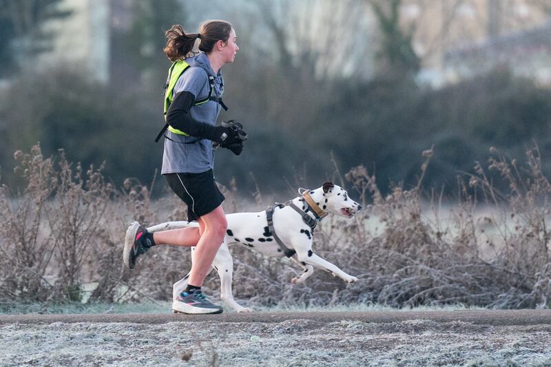 Dog and owner enjoy a morning run along the frosty bank of the River Cam in Cambridge at sunrise. PA