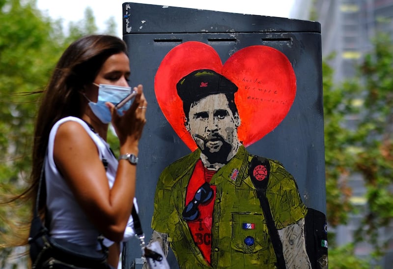 A woman wearing a protective face mask walks past a mural of Lionel Messi. Reuters