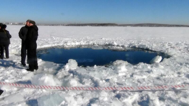 A handout photo taken on February 15, 2013, and provided by Chelyabinsk region police department shows people standing near a six-metre (20-foot) hole in the ice of a frozen lake, reportedly the site of a meteor fall, outside the town of Chebakul in the Chelyabinsk region. A plunging meteor exploded today with a blinding flash above central Russia, setting off a shock wave that shattered windows and hurt over 500 people in an event unprecedented in modern times. The office of the local governor said in a statement that a meteorite had fallen into a lake outside the town of Chebakul in the Chelyabinsk region. AFP PHOTO / CHELYABINSK REGION POLICE DEPARTMENT
-- RESTRICTED TO EDITORIAL USE - MANDATORY CREDIT "AFP PHOTO /  CHELYABINSK REGION POLICE DEPARTMENT" - NO MARKETING NO ADVERTISING CAMPAIGNS - DISTRIBUTED AS A SERVICE TO CLIENTS -- (Photo by - / CHELYABINSK REGION POLICE DEPART / AFP)