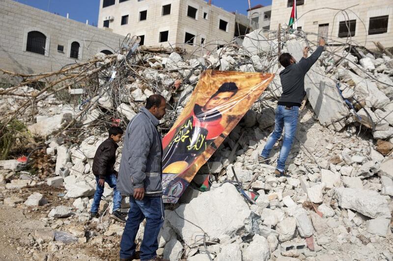 Muhanad Halabi's father, Shafiq, stands by the rubble of his family home that was destroyed by Israel, as his two sons Mustafa, 10, (L) and Mohammed, 21, secure a giant poster to the twisted metal showing a portrait of his late son in the Palestinian village of Surda on January 14, 2016. Photo by Heidi Levine For The National.

