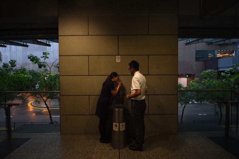 A woman tries to light a cigarette as workers shelter from winds from Typhoon Hato in Hong Kong's central district.
Heavy rains and driving winds lashed Hong Kong on August 23 shutting schools and the stock market and bringing chaos to the city's international airport where hundreds of flights were cancelled. Anthony Wallace / AFP.