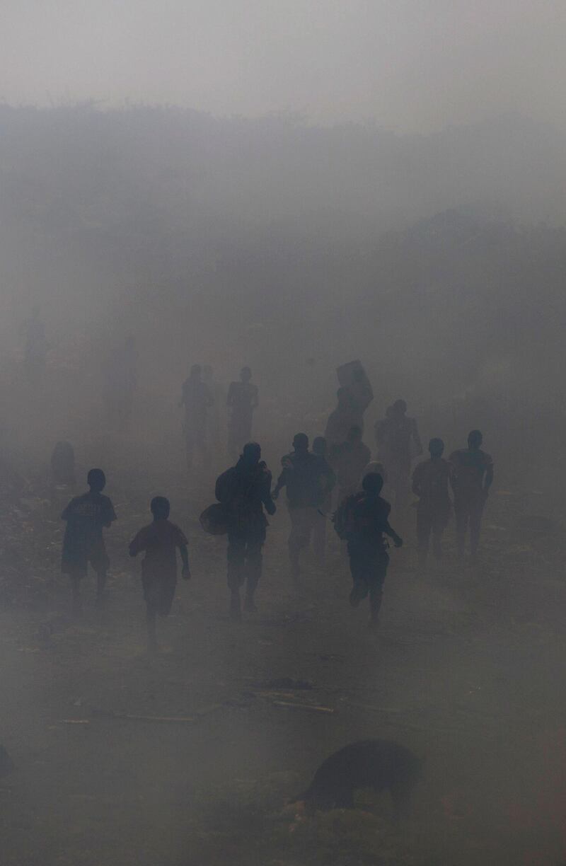 Trash scavengers run through the smoke of burning trash. AP Photo