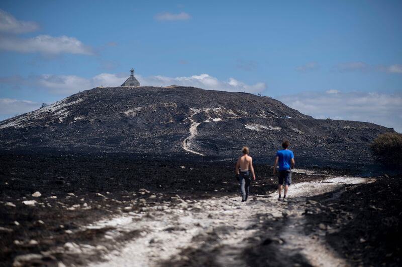 Two people walk on a path covered with ashes after a fire consumed acres of forest near Brasparts, western France.  AFP