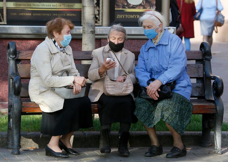 Elderly women wearing face masks to protect against coronavirus look at a phone sitting on a bench in Kiev, Ukraine. AP Photo