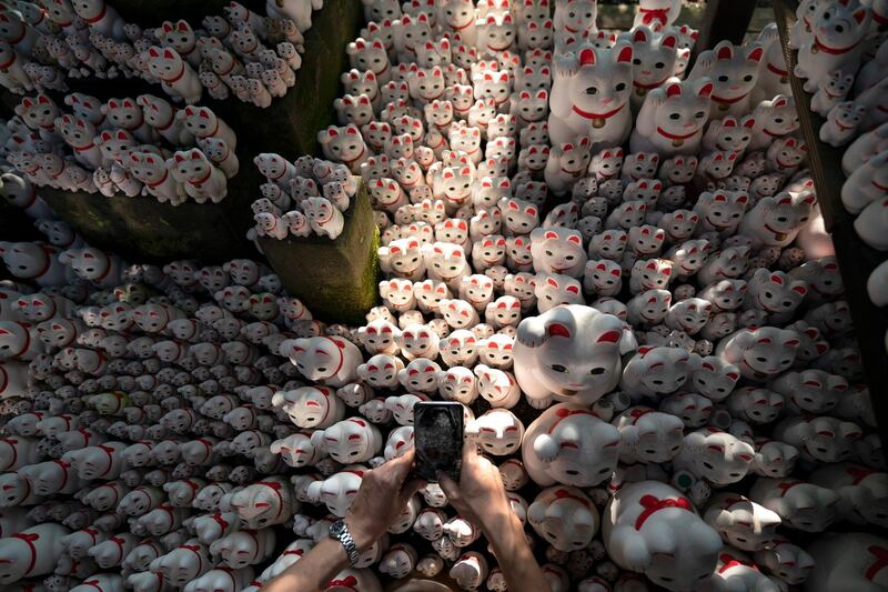 A visitor takes pictures of beckoning cat figurines at Gotokuji Temple in Tokyo.  AP