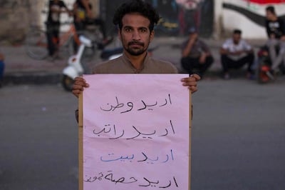 An Iraqi protester carries a placard which reads in Arabic "I want a homeland, I want a salary, I want a home, I want a share of provisions" during an anti-government demonstration in the southern city of Basra on November 13, 2020.  / AFP / Hussein FALEH
