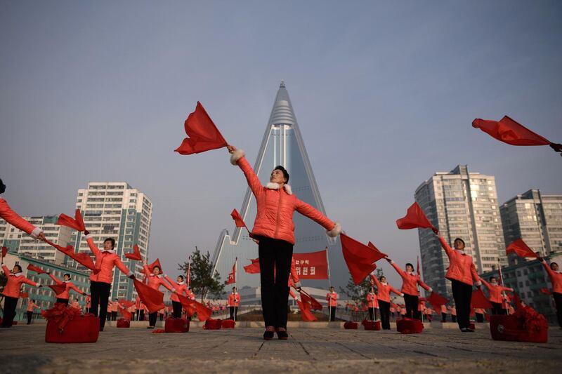 Members of a Socialist Women's Union propaganda troupe perform a dance and music routine in front of the Ryugyong hotel in Pyongyang.  All non-working North Korean women are members of the Socialist Women's Union, whose propaganda troupes are a familiar fixture performing flag-waving and drum routines at intersections and landmarks around Pyongyang during the morning rush-hour period.   AFP