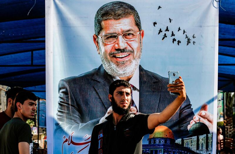 A Palestinian youth uses his phone to takes a "selfie" in front of a poster depicting the late former Egyptian president Mohamed Morsi in Khan Yunis in the southern Gaza Strip.  AFP