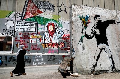 A Palestinian woman walks past fresh graffiti painted on Israel's controversial separation barrier in the occupied West Bank city of Bethlehem on June 22, 2018, by Palestinian street artist Taqi Sbateen depicting Razan Al Najjar (C), a paramedic nurse from Gaza who was killed by an Israeli sniper during a protest along the Israeli fence in Gaza. / AFP PHOTO / THOMAS COEX / RESTRICTED TO EDITORIAL USE - MANDATORY MENTION OF THE ARTIST UPON PUBLICATION - TO ILLUSTRATE THE EVENT AS SPECIFIED IN THE CAPTION