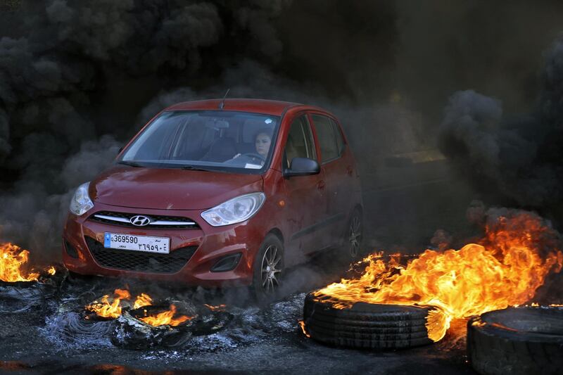 A woman drives through burning tires blocking a highway in Lebanon's northern port city of Byblos (Jbeil) during ongoing anti-government demonstrations. AFP