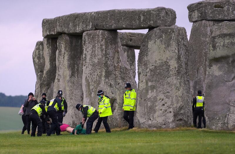 AMESBURY, ENGLAND - JUNE 21: People are removed by police officers after a crowd entered the closed site at Stonehenge on June 21, 2021, in Amesbury, United Kingdom. English Heritage, which manages the site, said, 'With this week's news that the Government is delaying the lifting of the remaining COVID-19 restrictions on 21 June we have taken the difficult decision to cancel the planned Summer Solstice celebrations at Stonehenge this year'. (Photo by Finnbarr Webster/Getty Images)