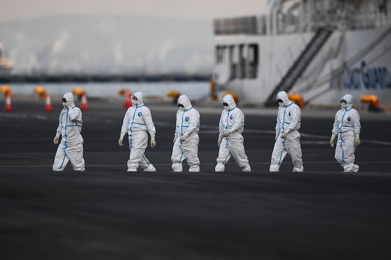 People wearing protective suits walk from the Diamond Princess cruise ship, with around 3,600 people quarantined onboard due to fears of the new coronavirus, at the Daikoku Pier Cruise Terminal in Yokohama port.  AFP