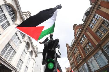 epa09202587 A supporters waves the Palestinian flag atop a traffic light pole during a demonstration outside the Israeli embassy in London, Britain, 15 May 2021. Israel Defense Forces (IDF) said they hit over 100 Hamas targets in the Gaza Strip during a retaliatory overnight strike after rockets were fired at Israel by Palestinian militants. EPA/FACUNDO ARRIZABALAGA