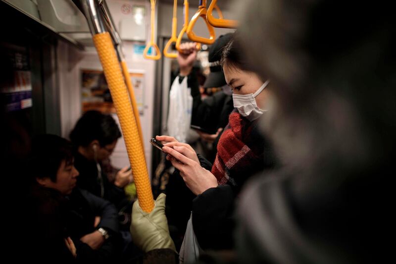 A woman wearing a facemask plays a video game on her smartphone on a subway train in Tokyo. AFP