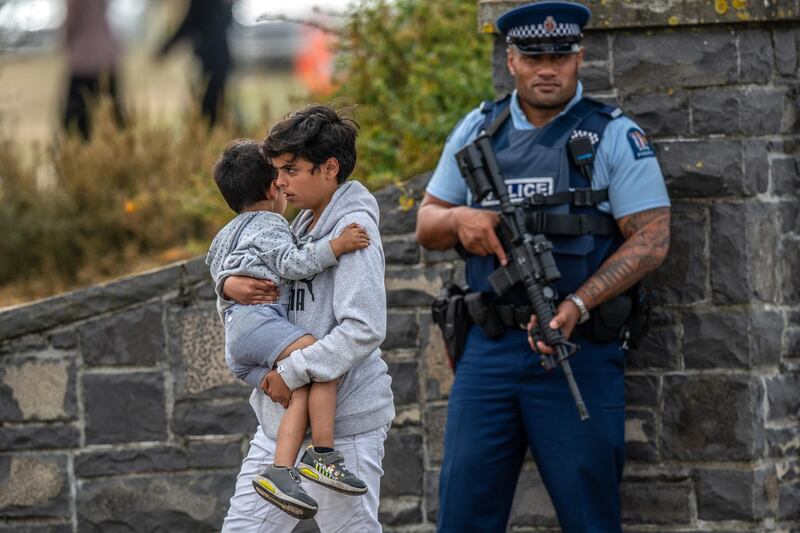 An armed policeman looks on as a youngster is carried by a boy as they leave Memorial Park Cemetery. Getty Images