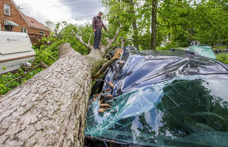 Michael Clark climbs onto a toppled tree to check out damage to three vehicles at his home in South Bend, Indiana. South Bend Tribune via AP