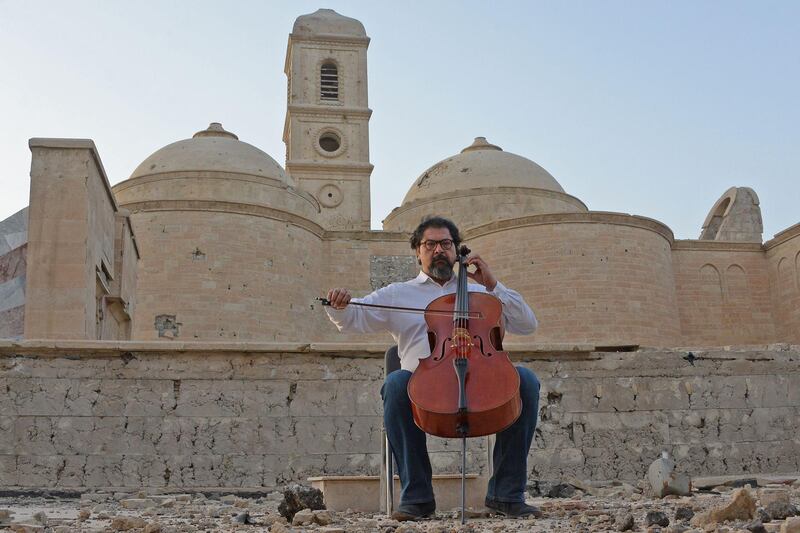 CORRECTION / Famed Iraqi maestro and cello player Karim Wasfi performs in front of the Roman Catholic Church of Our Lady of the Hour in Mosul’s war-ravaged Old City on June 29, 2018, one year after the mosque was destroyed during battles to retake the city from the Islamic State group. Wasfi is known for turning up with his cello to play in the aftermath of bombings in the capital Baghdad, alleviating pain through the soothing power of music. / AFP / Zaid AL-OBEIDI
