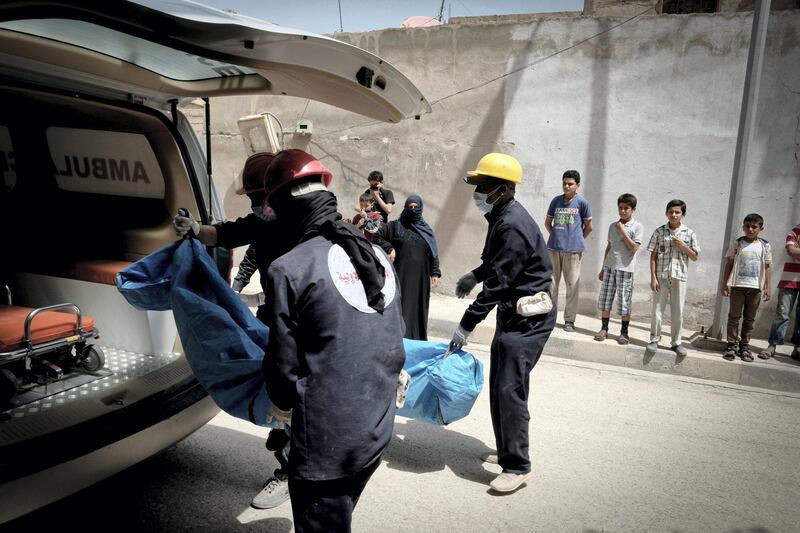 Children cover their faces against the smell of bodies as its loaded into ambulance in Raqqa. Photo: David Pratt for The National