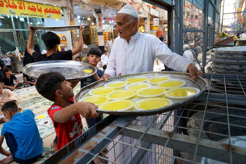 An Iraqi man with the help of a young boy carries plates filled with delicacies as people gather to break their fast at a free communal iftar in the central Iraqi city of Najaf. Reuters