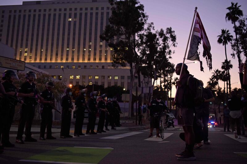 A man faces a row of police holding a burnt upside-down US flag as protesters gather in downtown Los Angeles. AFP