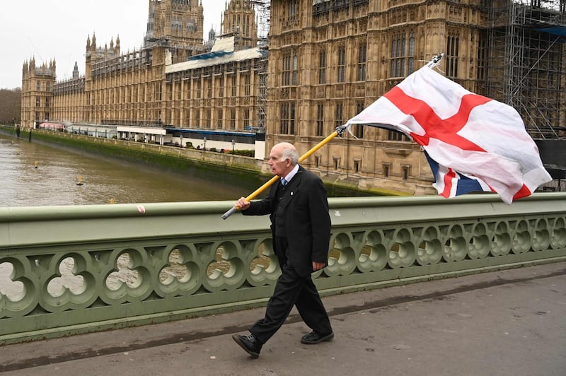 A man carries a flag of St George, the English national flag, along with a Union Flag as he walks along Westminster Bridge. AFP