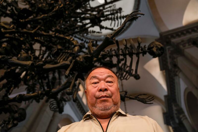 Chinese artist Ai Weiwei poses in front of his unveil glass body of work 'La Commedia Umana' a huge hanging glass sculpture otherwise referred to as a 'chandelier' at the San Giorgio deconsecrated church in Venice, Italy, Friday, Aug.  26, 2022.  Chinese artist Ai Weiwei lampoons the surveillance culture and social media with his first ever glass sculpture, made on the Venetian island of Murano, that stands as a warning to the world: "Memento Mori,'' or Latin for "Remember You Must Die. " (AP Photo / Luca Bruno)