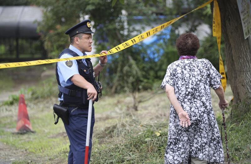 A police officer patrols the perimeter of the scene with an elderly resident looking on. Eugene Hoshiko / AP Photo