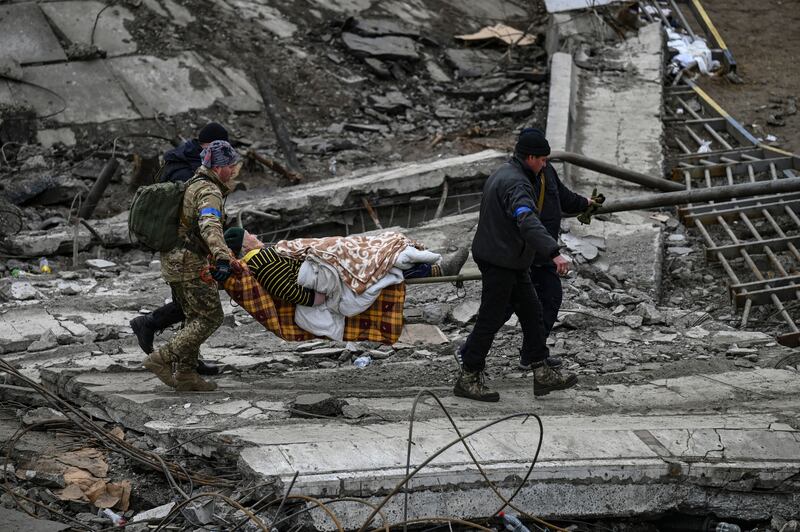 Ukrainian servicemen carry an elderly woman on a stretcher from the city of Irpin. AFP