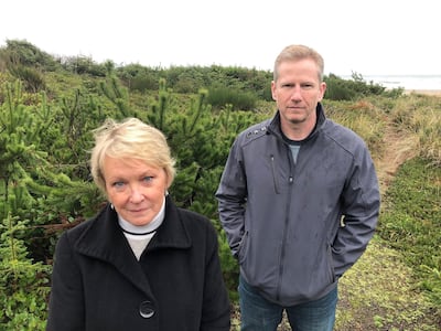 Patricia Rogers, left, and Jeff Bryner, who each have houses next to a lot that a Facebook subsidiary bought for a landing site for a trans-Pacific fiber optic cable, pose during an interview on Wednesday, Jan. 8, 2020, with the Facebook lot behind them, in Tierra Del Mar, Ore. They and other residents of the tiny community on the Oregon coast strongly oppose the Facebook project, fearing it will change their community. (AP Photo/Andrew Selsky)