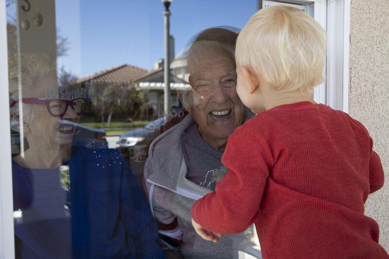 A child in California greets his elderly neighbour through a window, adhering to social distancing rules, on April 3, 2020. AFP