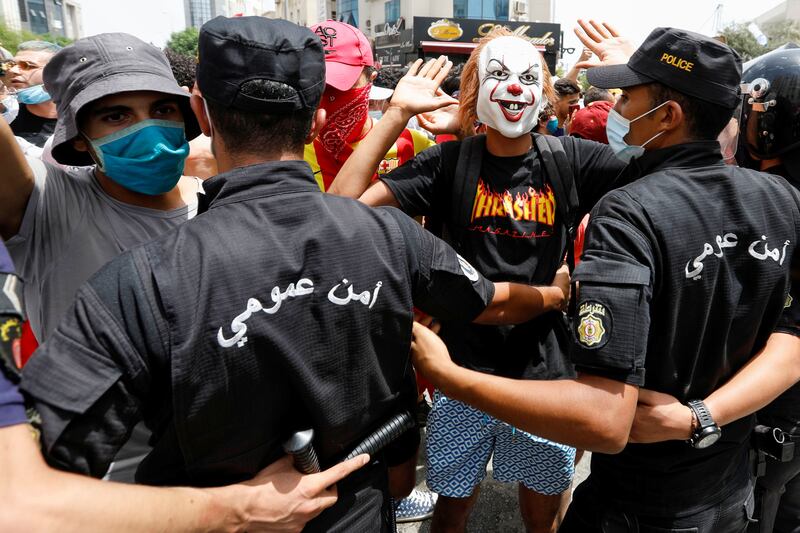 A demonstrator wearing a mask gestures in front of police officers standing guard during the anti-government protest.