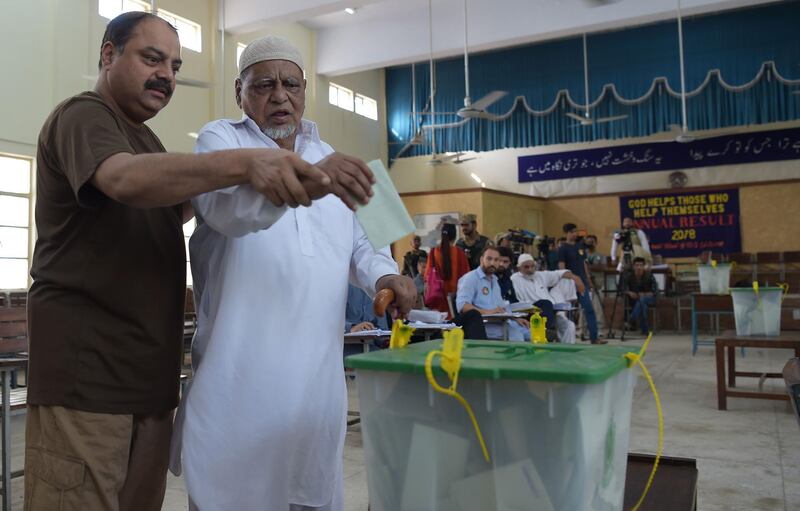 A Pakistani man helps his blind father to casts his vote at a polling station during Pakistan's general election in Islamabad on July 25, 2018. Pakistanis vote on July 25 in elections that could propel former World Cup cricketer Imran Khan to power, as security fears intensified with a voting-day blast that killed at least 30 after a campaign marred by claims of military interference. / AFP / AAMIR QURESHI
