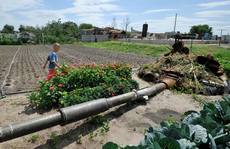 A boy walks in a garden past the wreckage of a Russian battle tank, destroyed during battles this spring, in the village of Velyka Dymerka, Ukraine. AFP