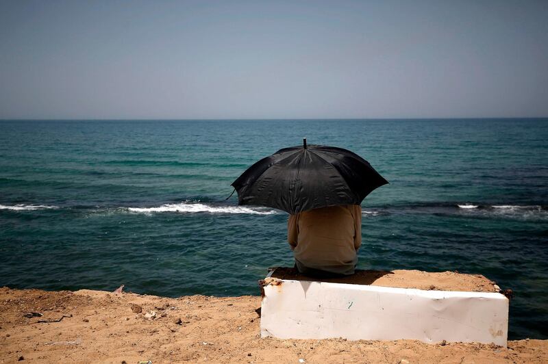 A Palestinian sits beneath an umbrella by the shoreline of a beach in Gaza City. AFP