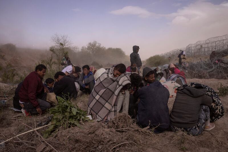 Migrants huddle on the dry riverbed of the Rio Grand as they endure heavy winds and dust while searching for an entrance into the US past a fortified razor wire-laden fence in El Paso, Texas. Reuters