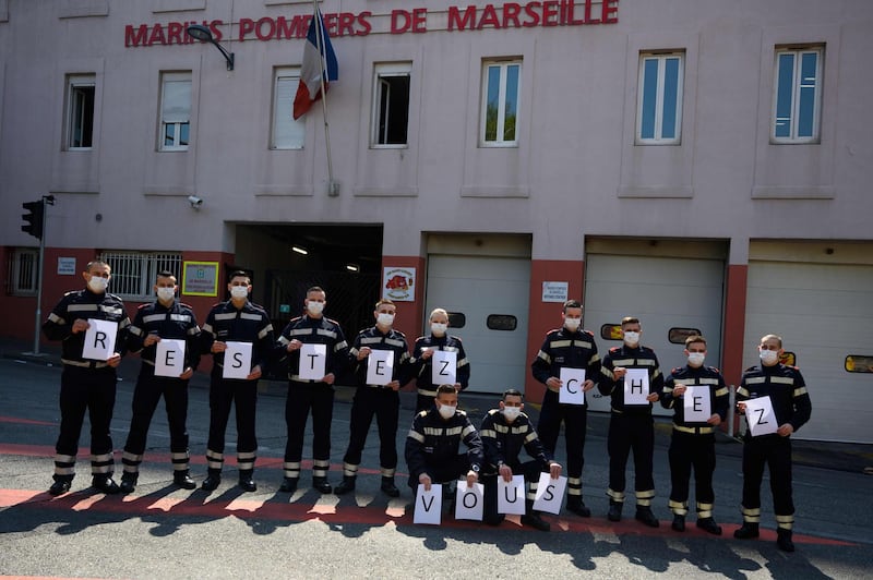TOPSHOT - French firefighters from Marin unit of Marseille wearing protective masks hold placards reading " Stay at home "  at the Saint Lazare barracks in Marseille on 03 April, 2020, during the strict lockdown in France to stop the spread of the novel coronavirus.  / AFP / Christophe SIMON
